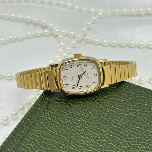 Dainty classic square dial gold tone Timex watch with quartz movement and stretchable band.