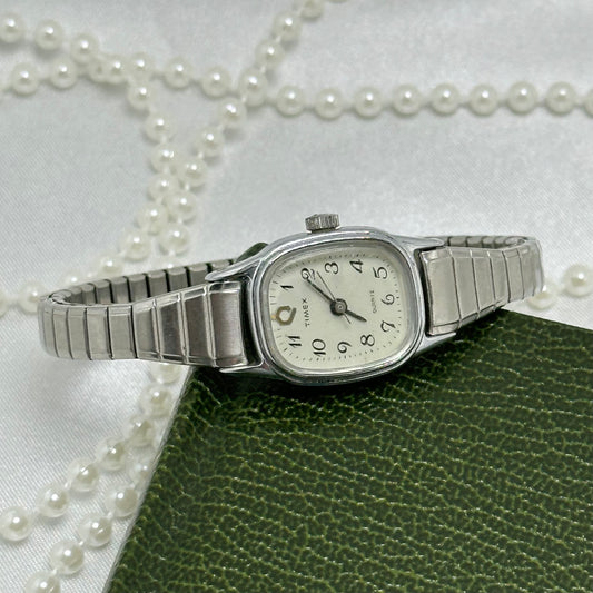 Dainty classic square dial silver tone Timex watch with quartz movement and stretchable band.