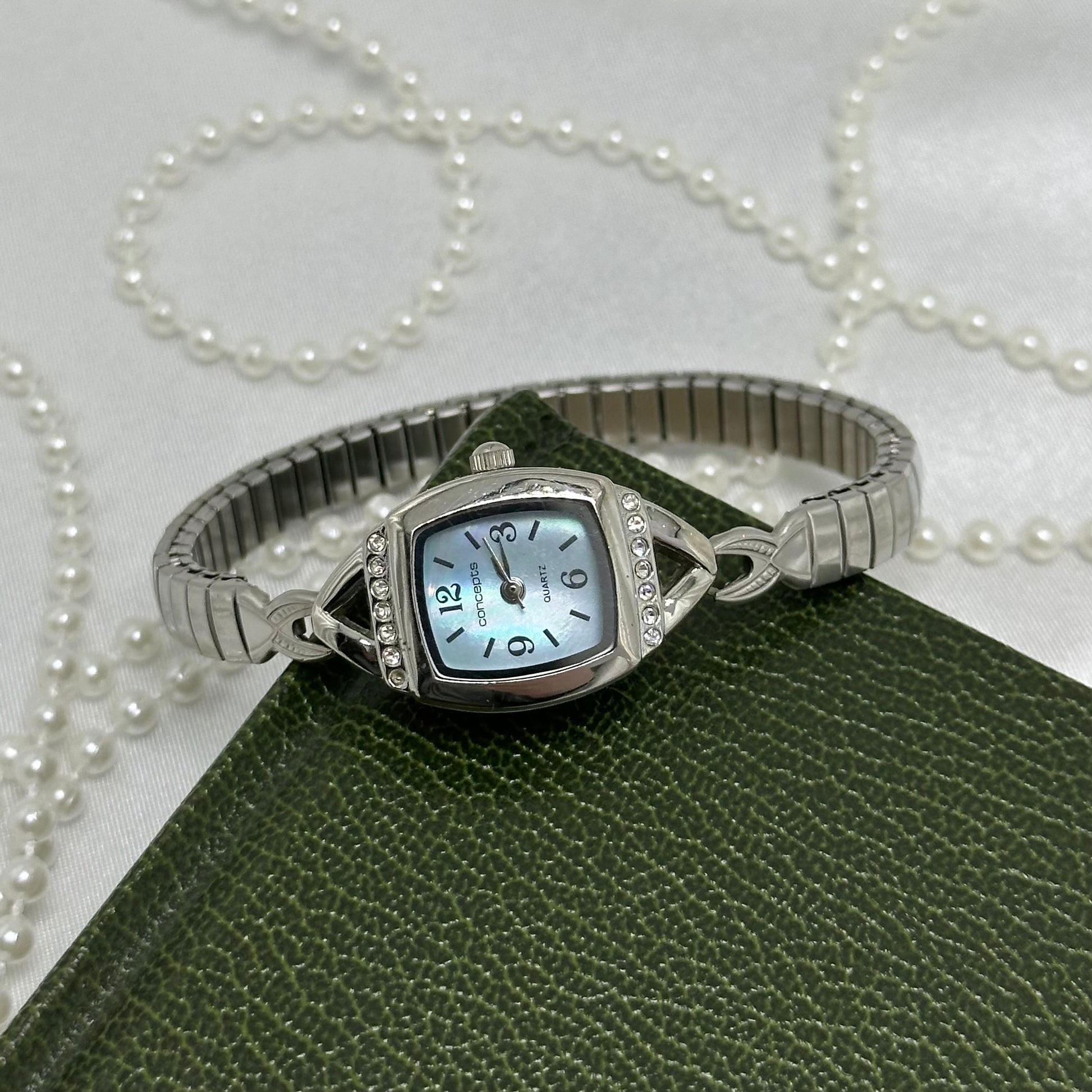 Dainty silver tone Concepts watch with square diamanté mother of pearl dial and stretchable band.