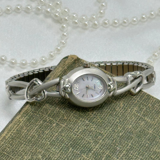 Dainty silver tone watch with heart band and quartz movement. Dial is mother of pearl.