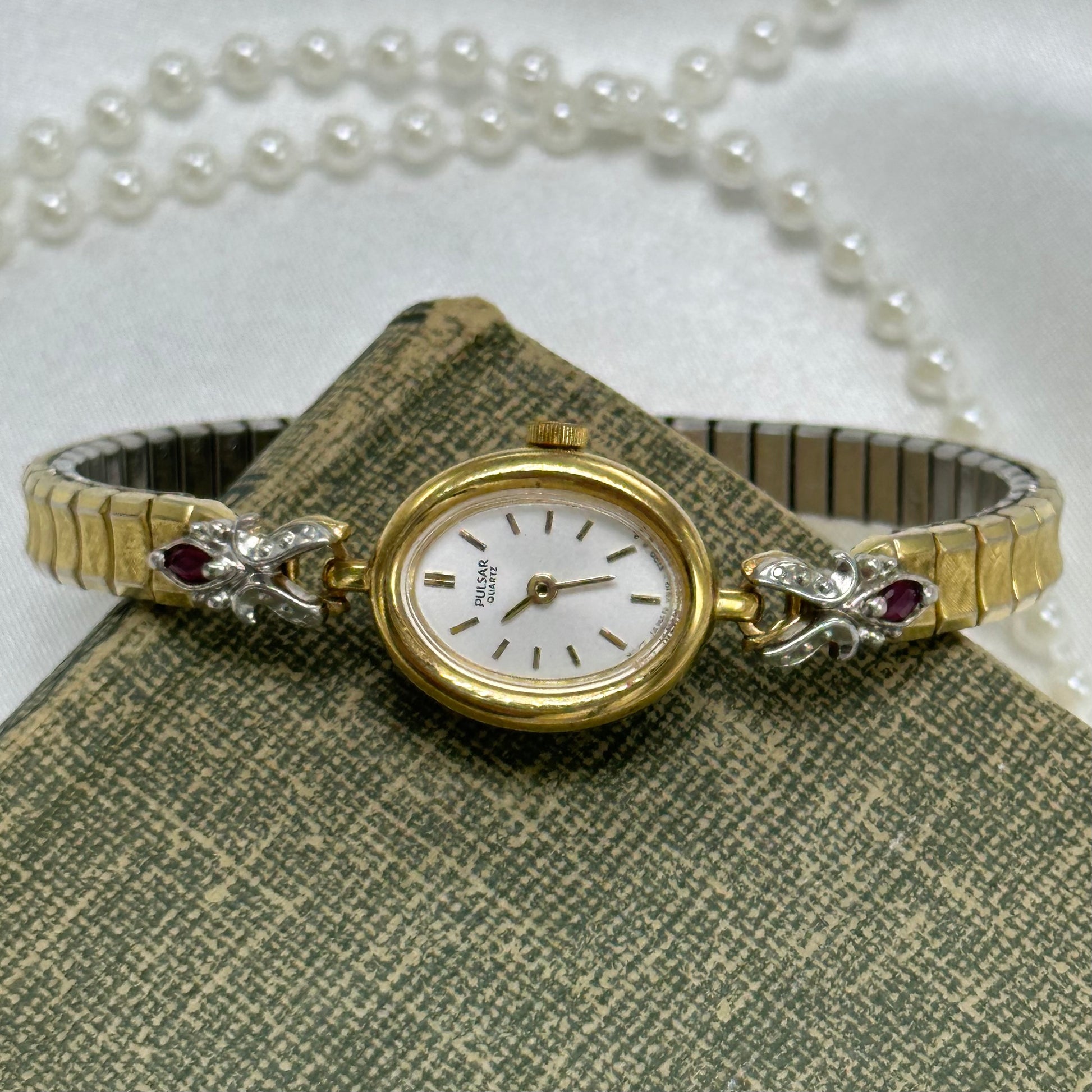 Dainty vintage gold tone oval dial Pulsar watch with quartz movement and synthetic ruby band.