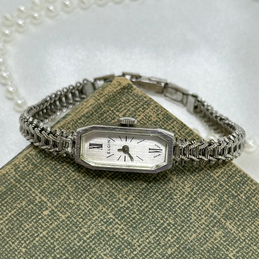 Dainty vintage silver tone manual winding Elgin watch with unique chain band and rectangle dial.