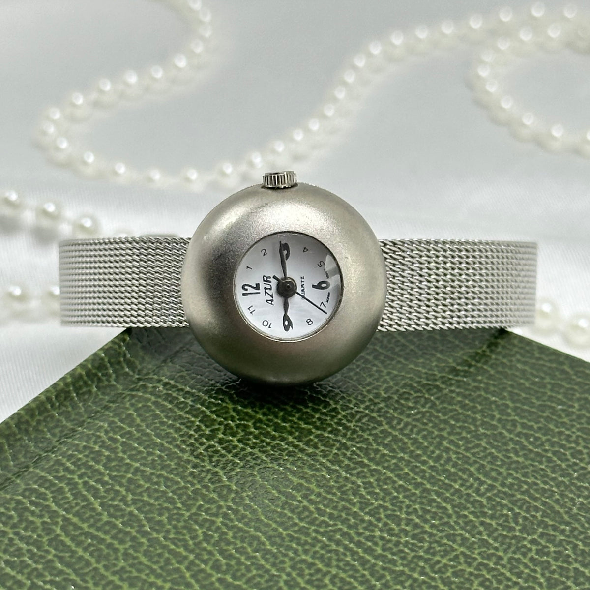 Dainty silver tone CM watch with cute bubble dial and slender metal mesh band.