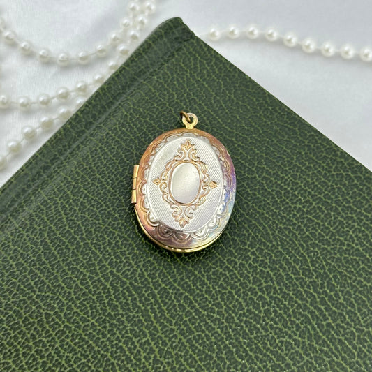 Gold/rose gold tone oval locket with filigree details engraved. Has tone loss.