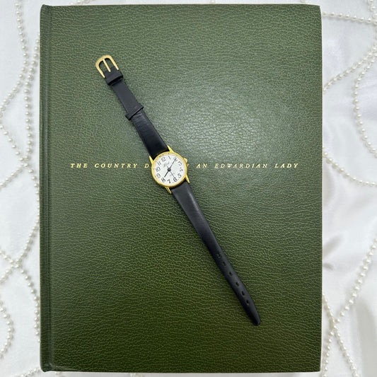 Gold tone LTD round dial watch with quartz movement and black leather band.