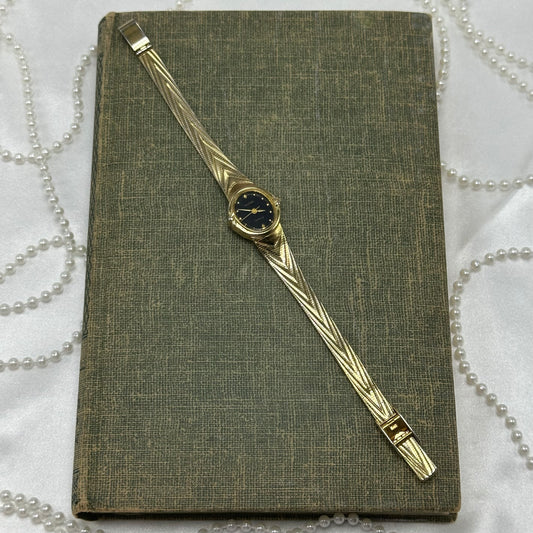 Gold tone Waltham watch with black dial and quartz movement.