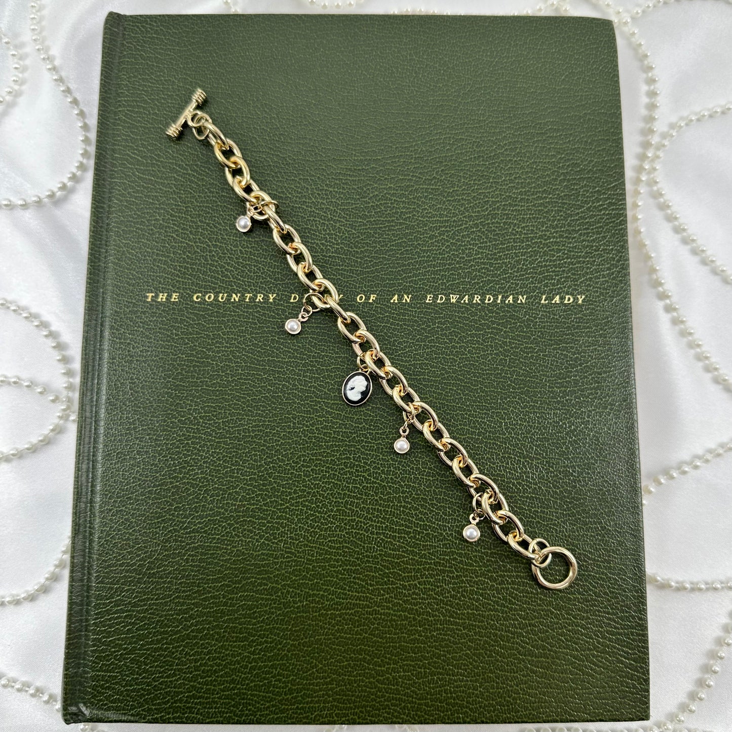 Gold tone chunky chain charm bracelet with faux pearls, black cameo, and t-bar style clasp.