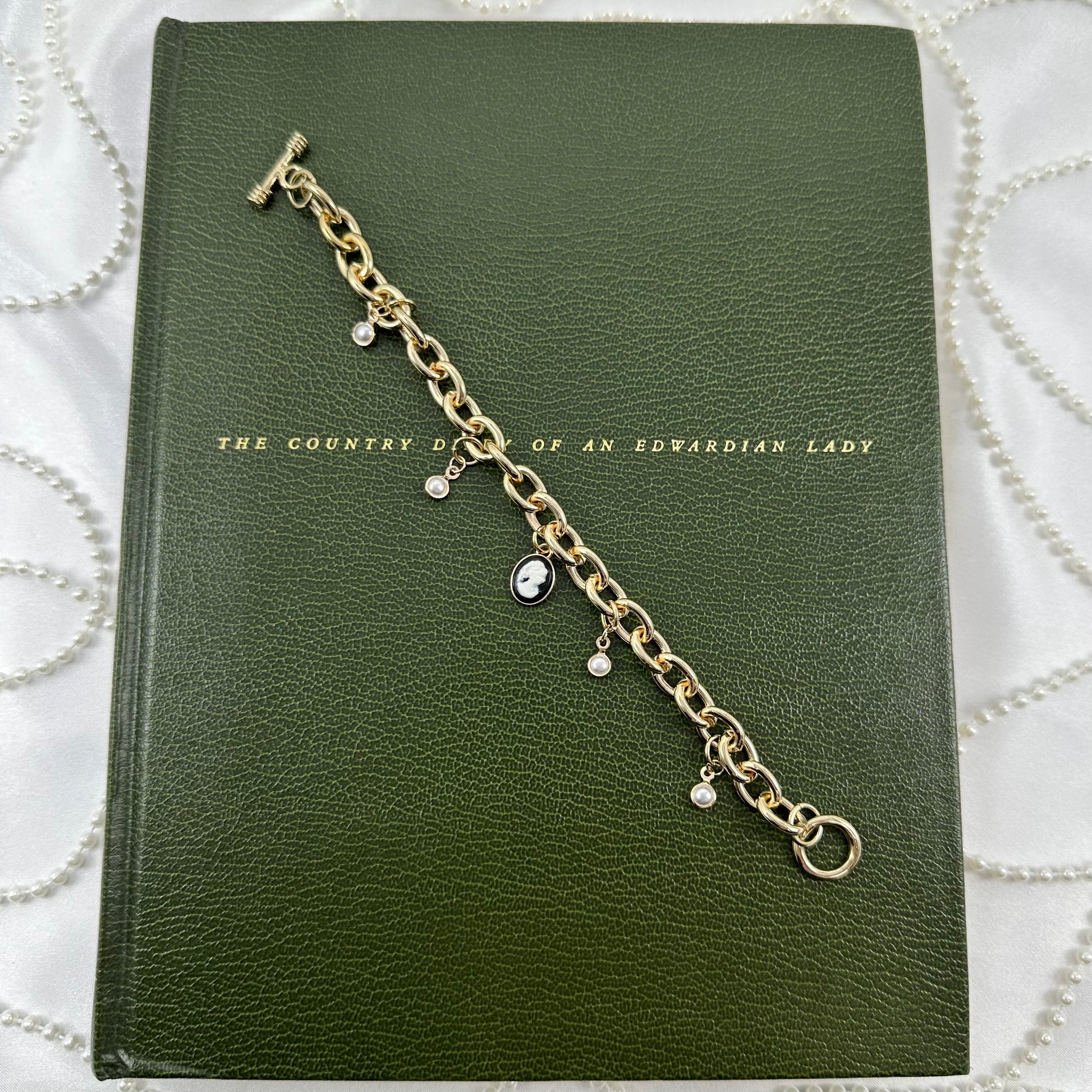 Gold tone chunky chain charm bracelet with faux pearls, black cameo, and t-bar style clasp.