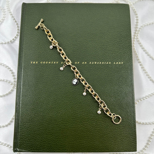 Gold tone chunky chain charm bracelet with faux pearls, black cameo, and t-bar style clasp.
