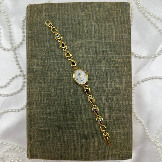 Gold tone multicolor stone watch with mother of pearl dial and quartz movement.