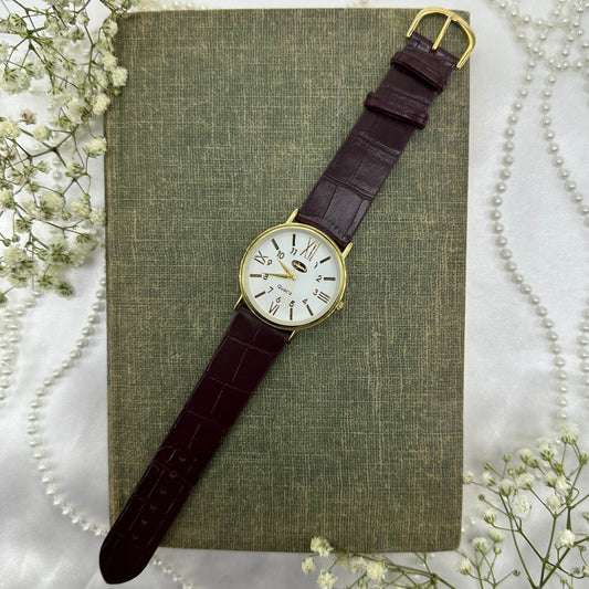 Gold tone round dial Cambridge watch with quartz movement and faux leather band.