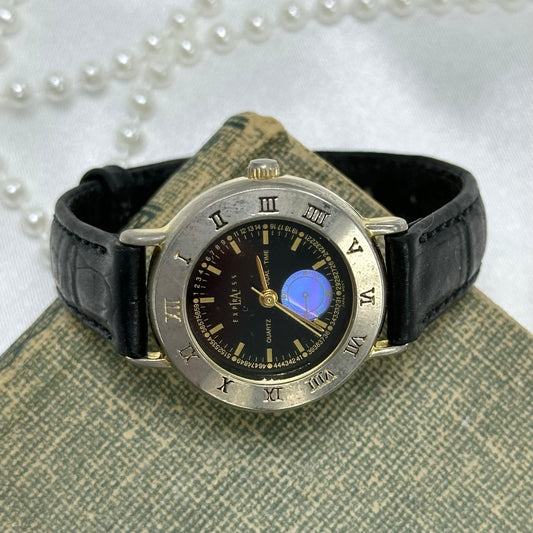 Gold tone round dial LA Express Dual-Time watch with roman numeral markers and black leather band. Second dial is iridescent