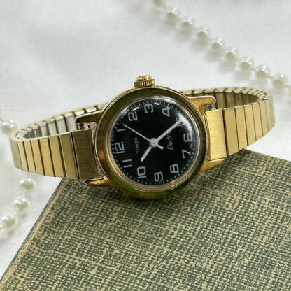 Gold tone vintage Timex electric watch with black dial and stretchable band.