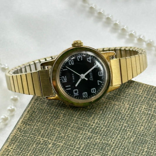 Gold tone vintage Timex electric watch with black dial and stretchable band.