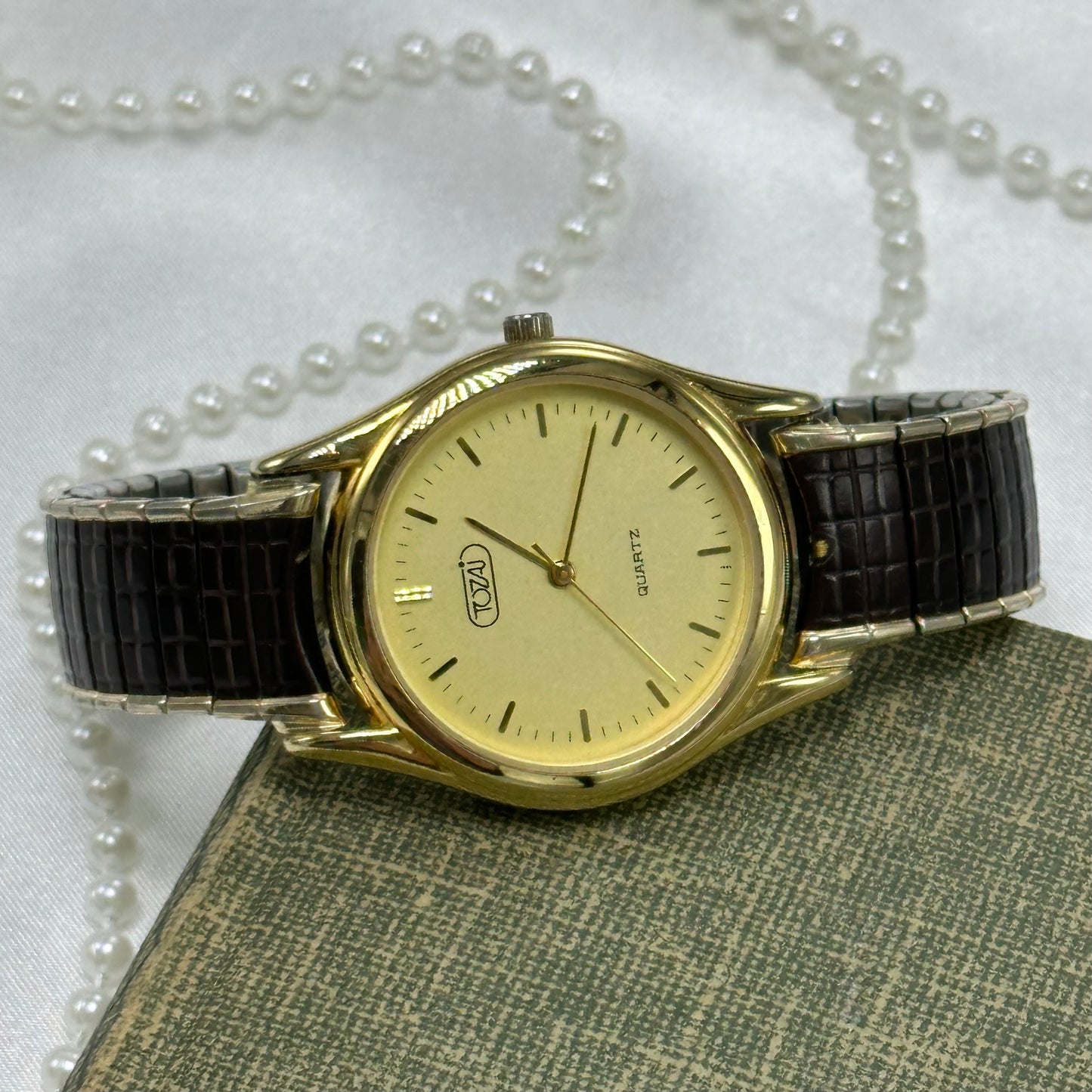 Gold tone vintage round dial Tozai watch with brown stretchable band and quartz movement.