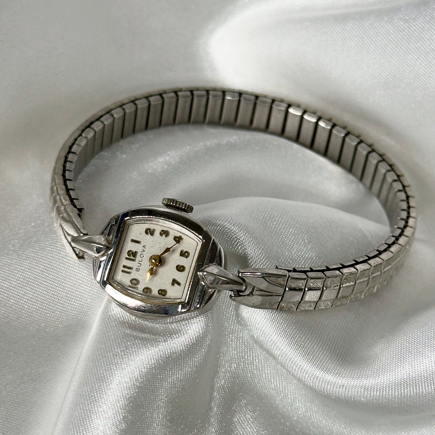 Silver Tone Bulova manual winding watch with stretchable band. Hands and markers on the dial are gold