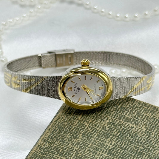 Silver and gold tone Wrangler watch with two-tone floral clasp band and gold oval dial.