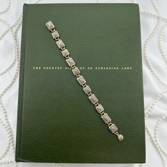 Silver and gold tone metal bracelet with textured, rectangles and square design. Clasp is magnetic.