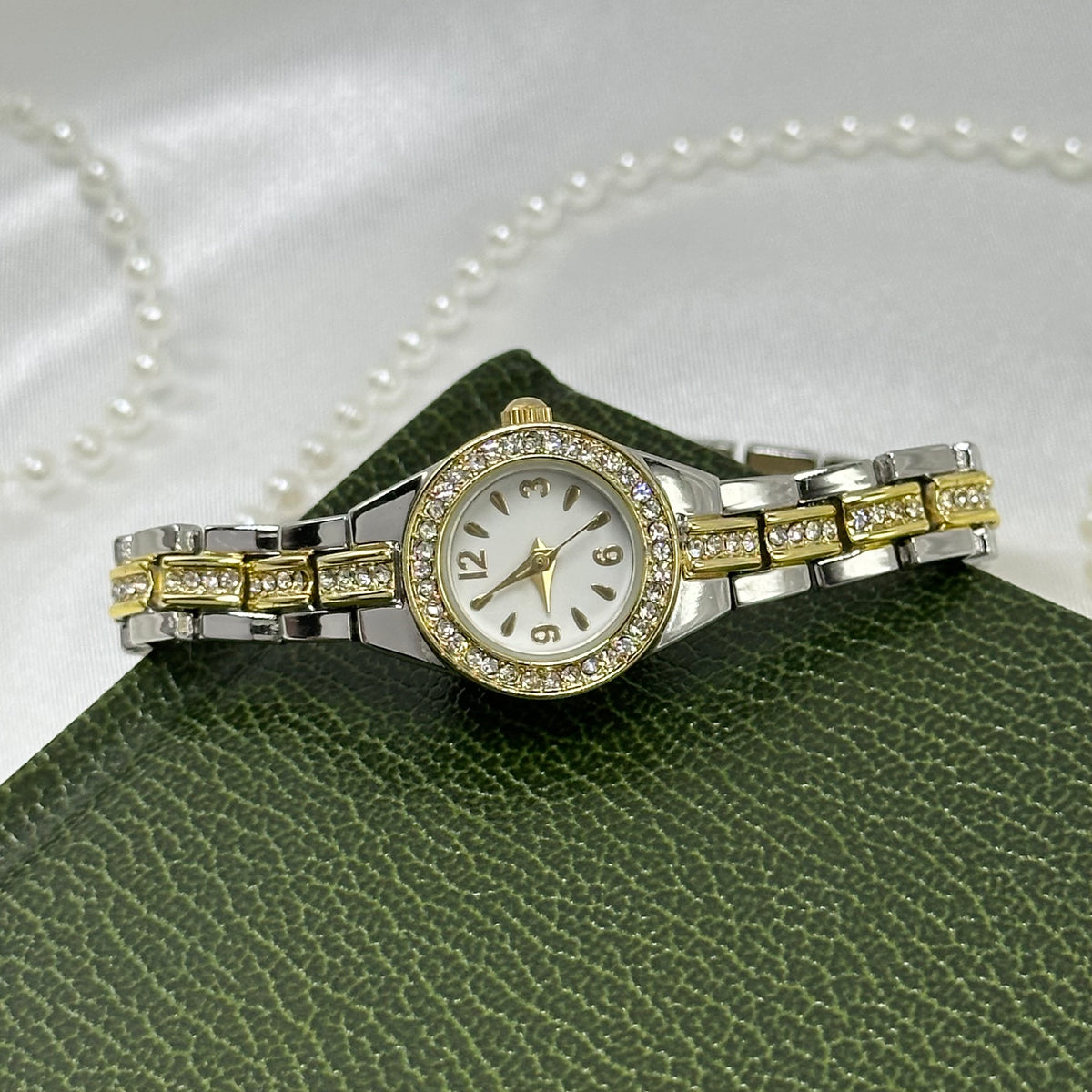 Silver and gold tone slender watch with diamanté round dial and two-tone metal clasp band.