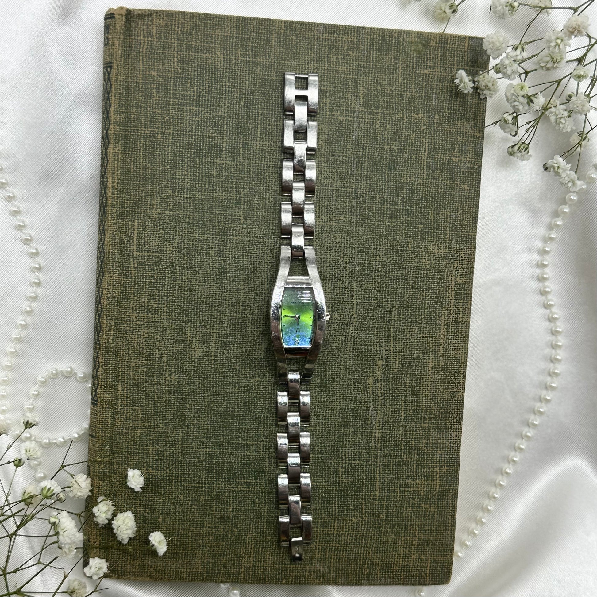 Silver tone Fossil watch with blue and green iridescent dial and clasp band.