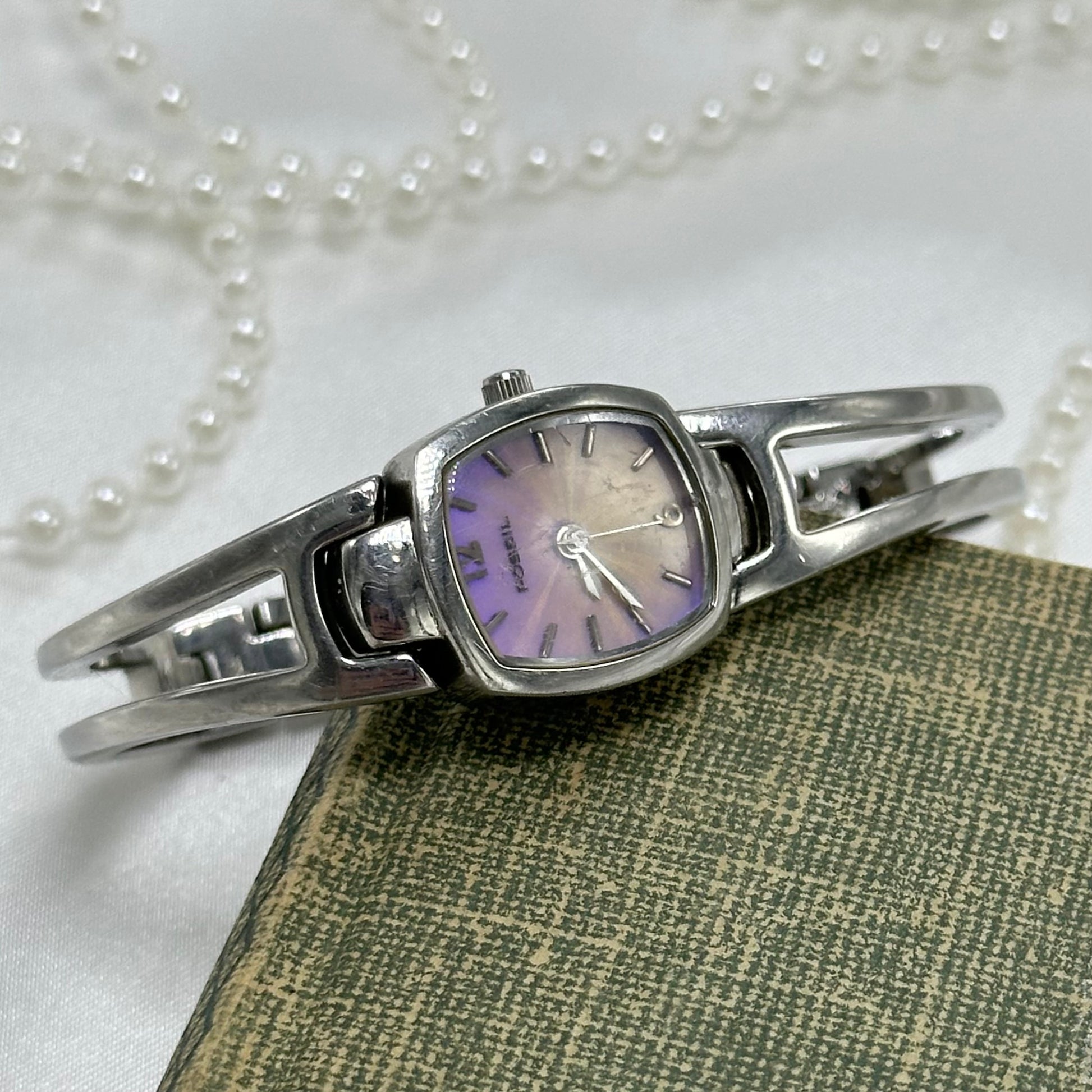 Silver tone Fossil watch with cuff band and quartz movement. Dial is iridescent.