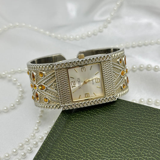 Silver tone Studio Time cuff watch with square dial. Detailed textured band with orange/amber gemstones.