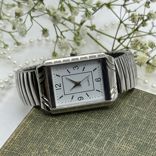 Silver tone rectangle dial watch with quartz movement and stretchable band.