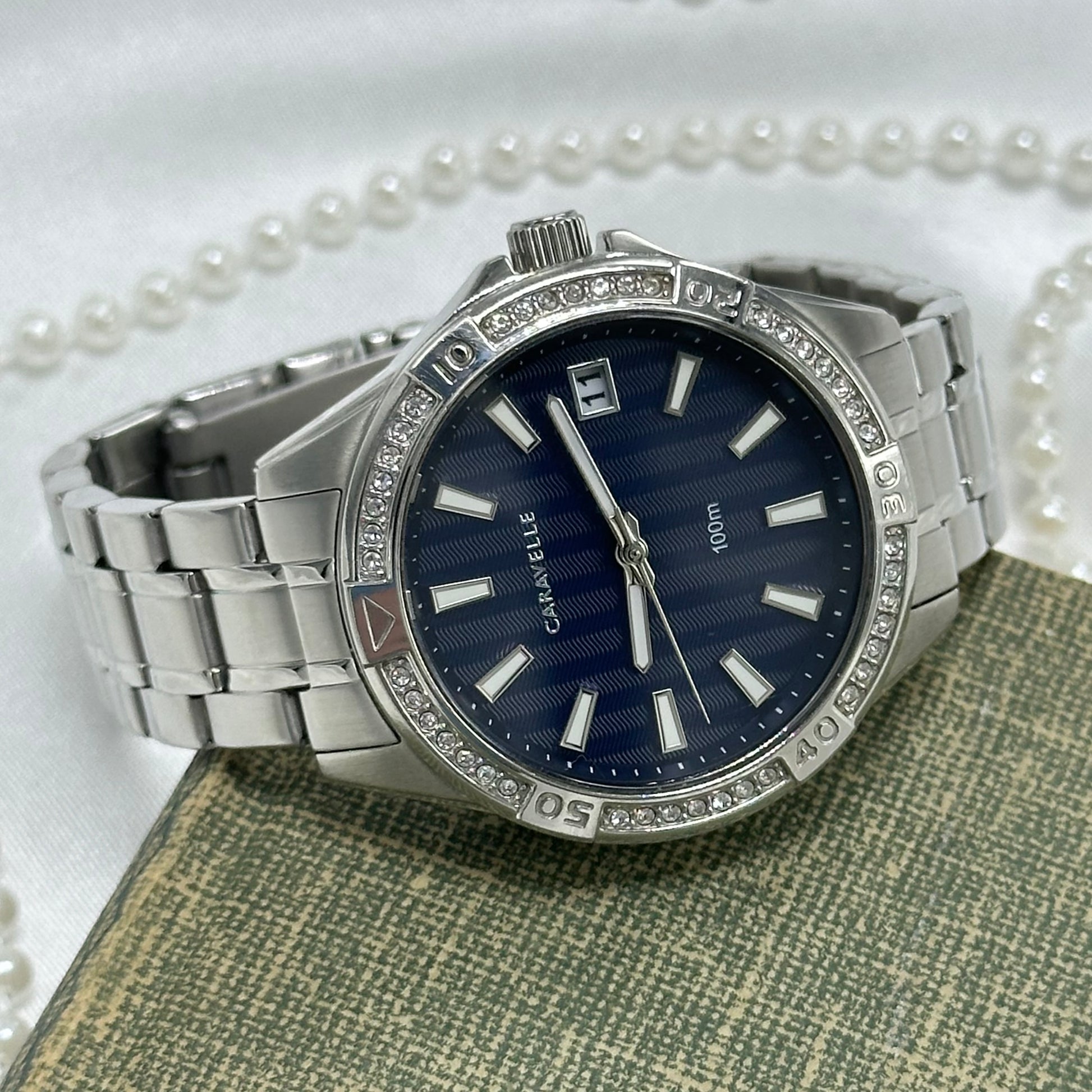Silver tone stainless steel diamanté navy blue dial Caravelle by Bulova watch with double locking fold over clasp and date display. Water resistant up to 330 ft (100 meters).