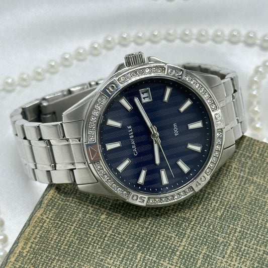 Silver tone stainless steel diamanté navy blue dial Caravelle by Bulova watch with double locking fold over clasp and date display. Water resistant up to 330 ft (100 meters).