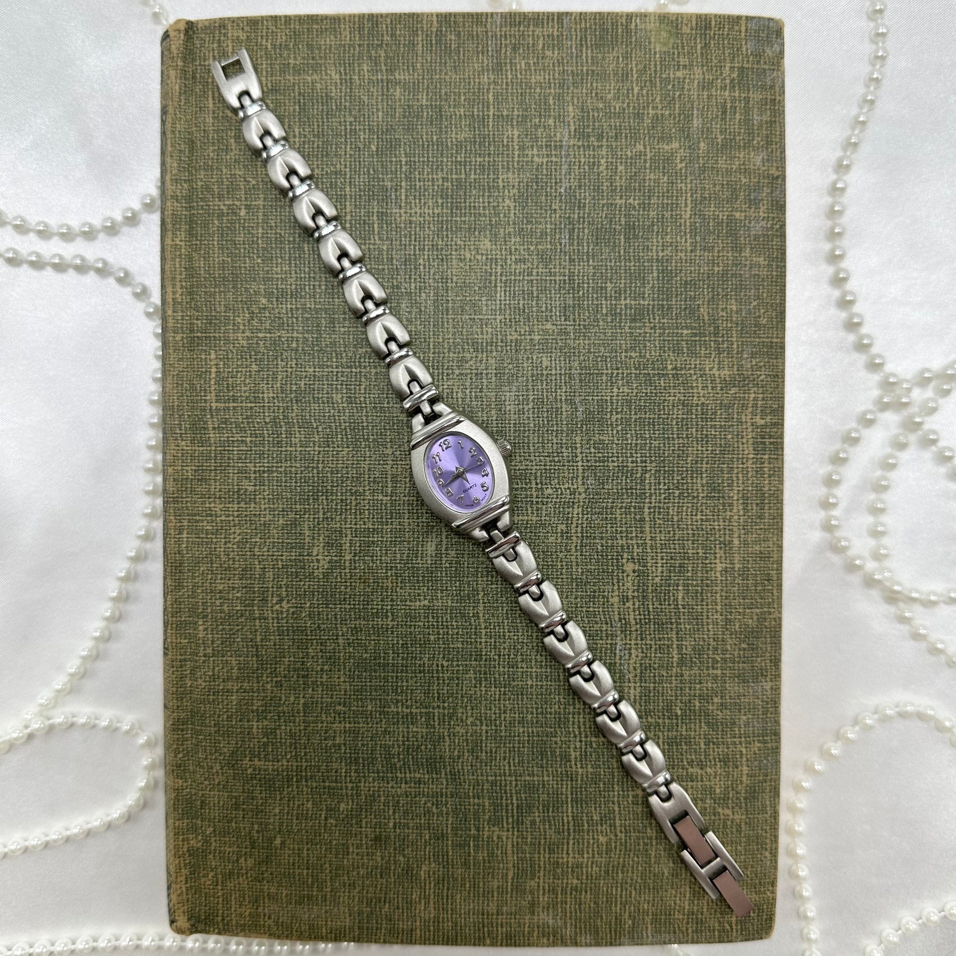 Silver tone watch with purple dial and quartz movement.