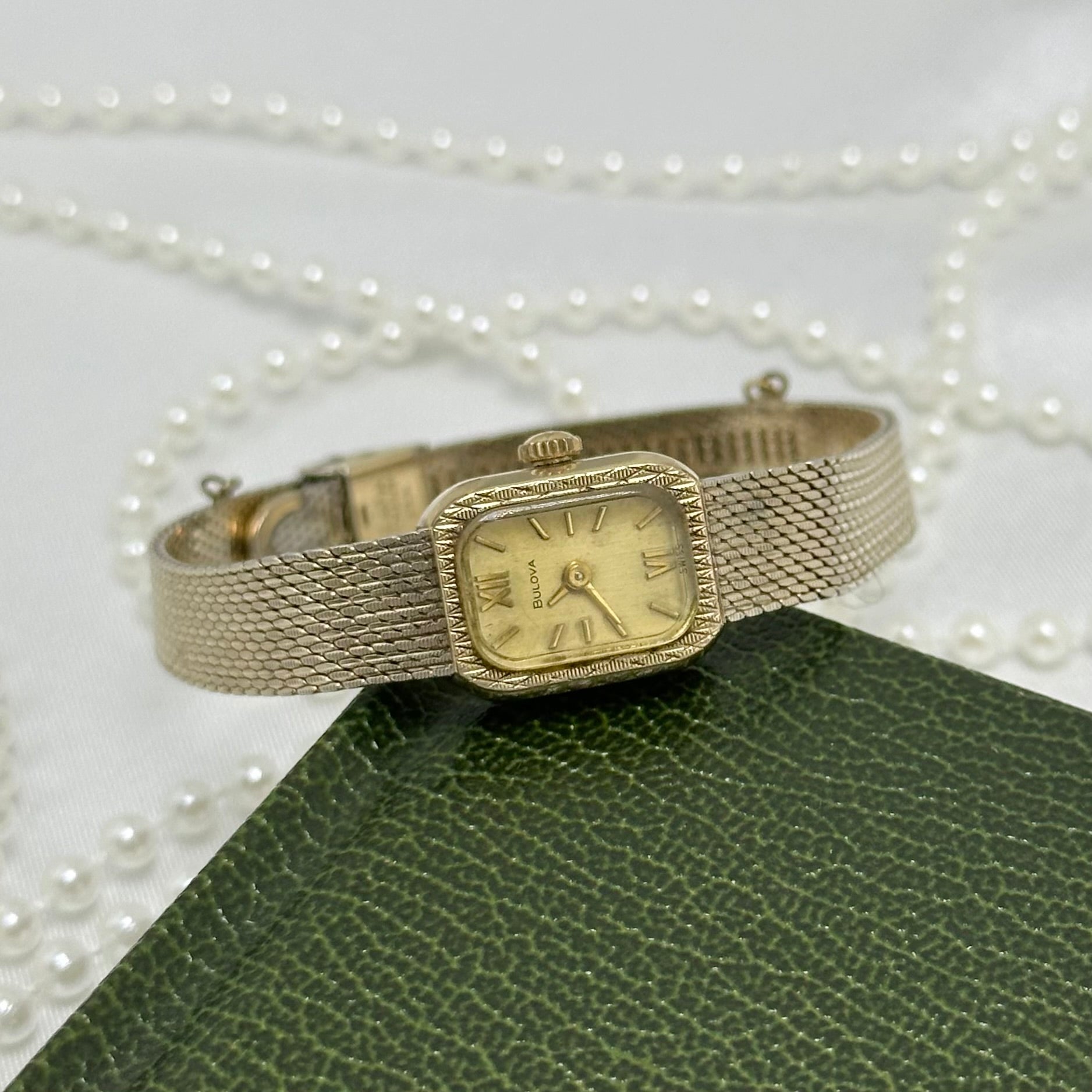 Vintage 10k rolled gold plated Bulova Swiss made manual winding watch with adjustable clasp band, roman numeral markers and rectangular dial from 1970.