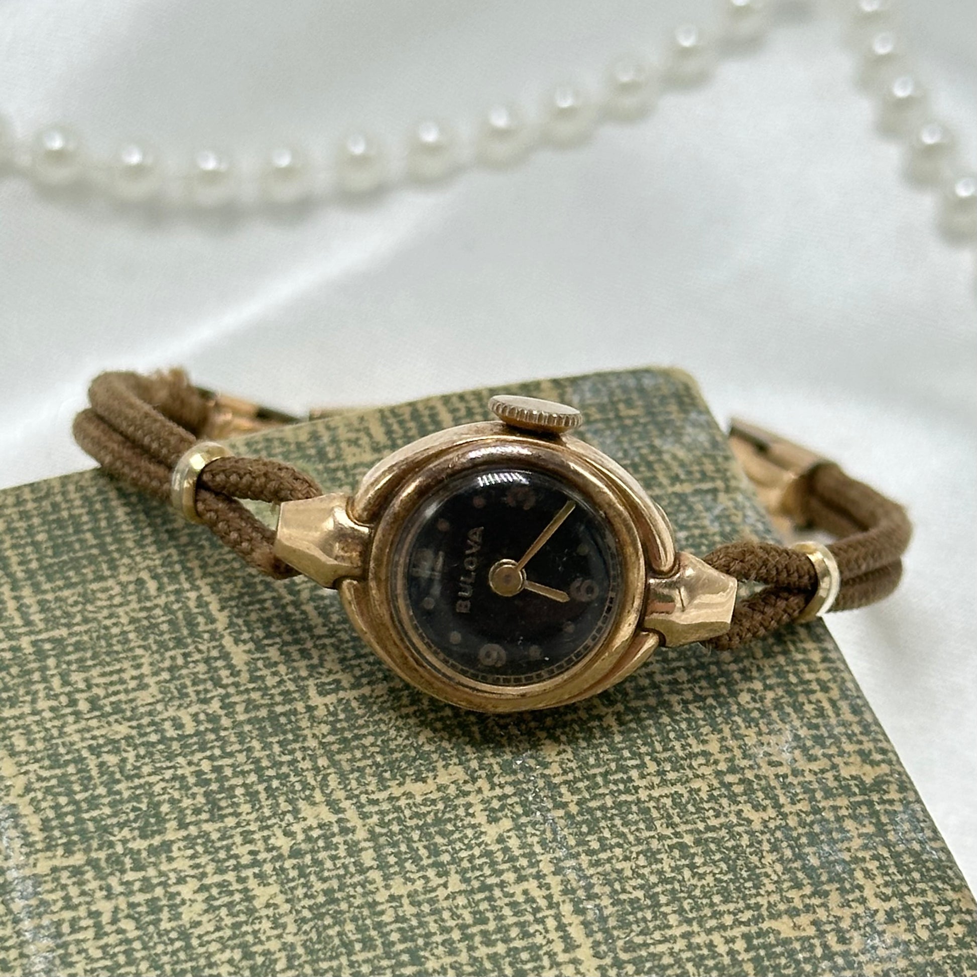 Vintage 14k gold bezel Bulova manual winding watch with dainty black dial and soft brown band. Clasp is 12k gold filled.