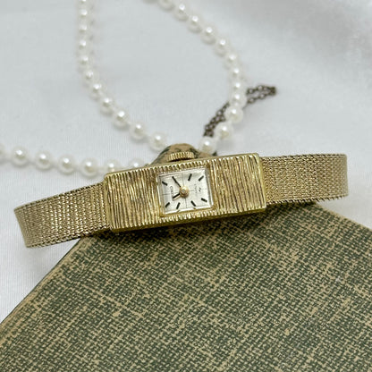 Vintage dainty gold tone manual winding Seiko 17 jewels manual winding watch with slender detailed band and safety chain.