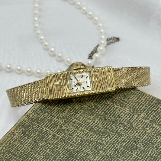 Vintage dainty gold tone manual winding Seiko 17 jewels manual winding watch with slender detailed band and safety chain.