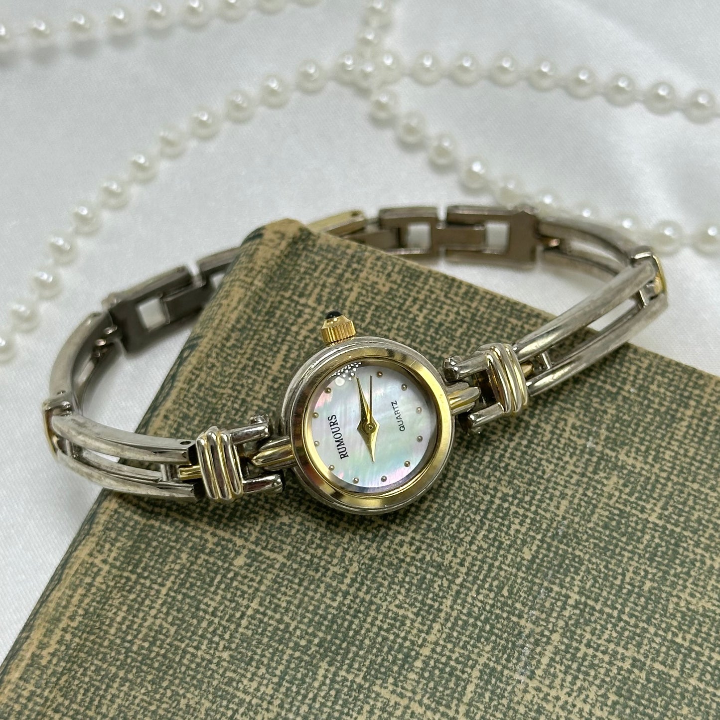 Vintage gold and silver tone Rumours watch with dainty round mother of pearl dial and two-tone band/bezel. Crown is a blue jewel.