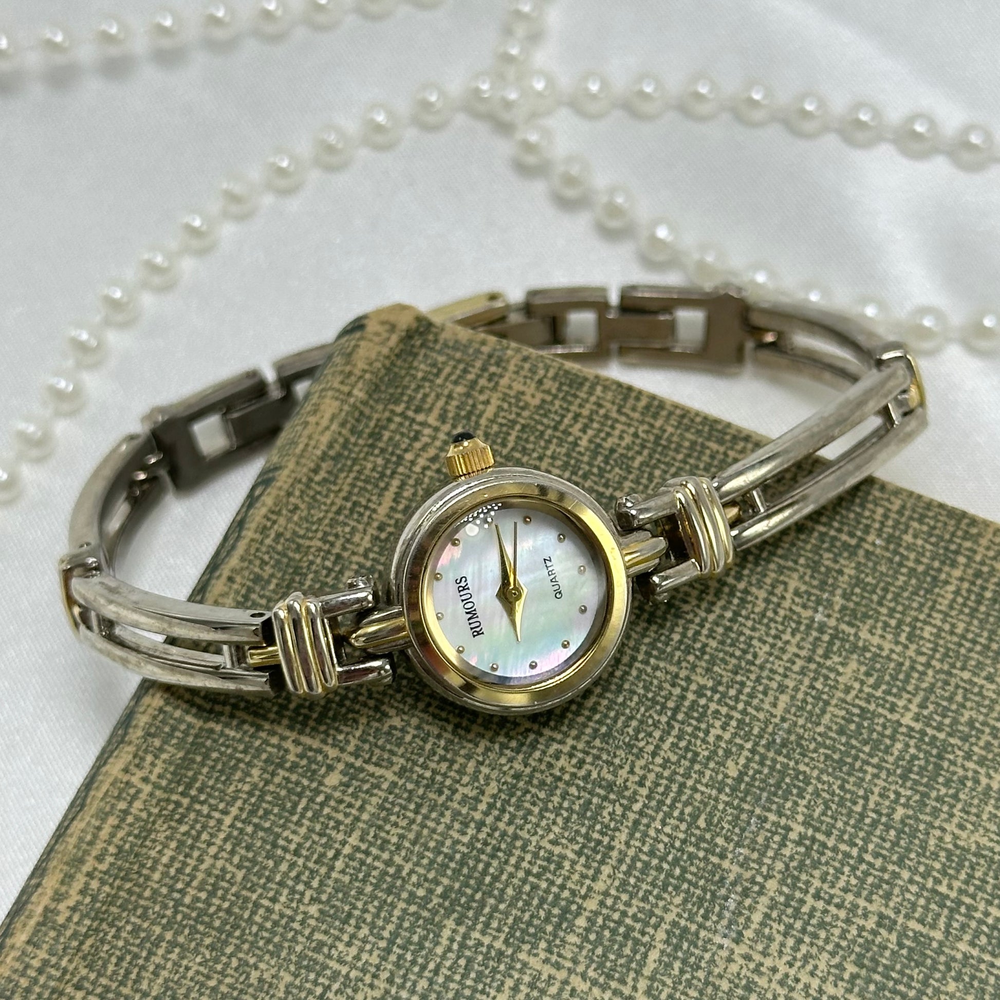 Vintage gold and silver tone Rumours watch with dainty round mother of pearl dial and two-tone band/bezel. Crown is a blue jewel.