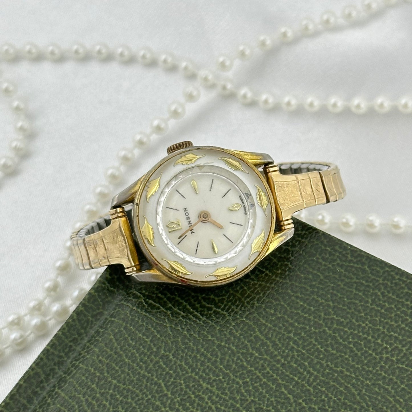 Vintage gold plated Manson Swiss manual winding watch with stunning white dial with gold accents, decorative leaf motifs on the bezel and detailed gold filled stretchable band from the 1950's.