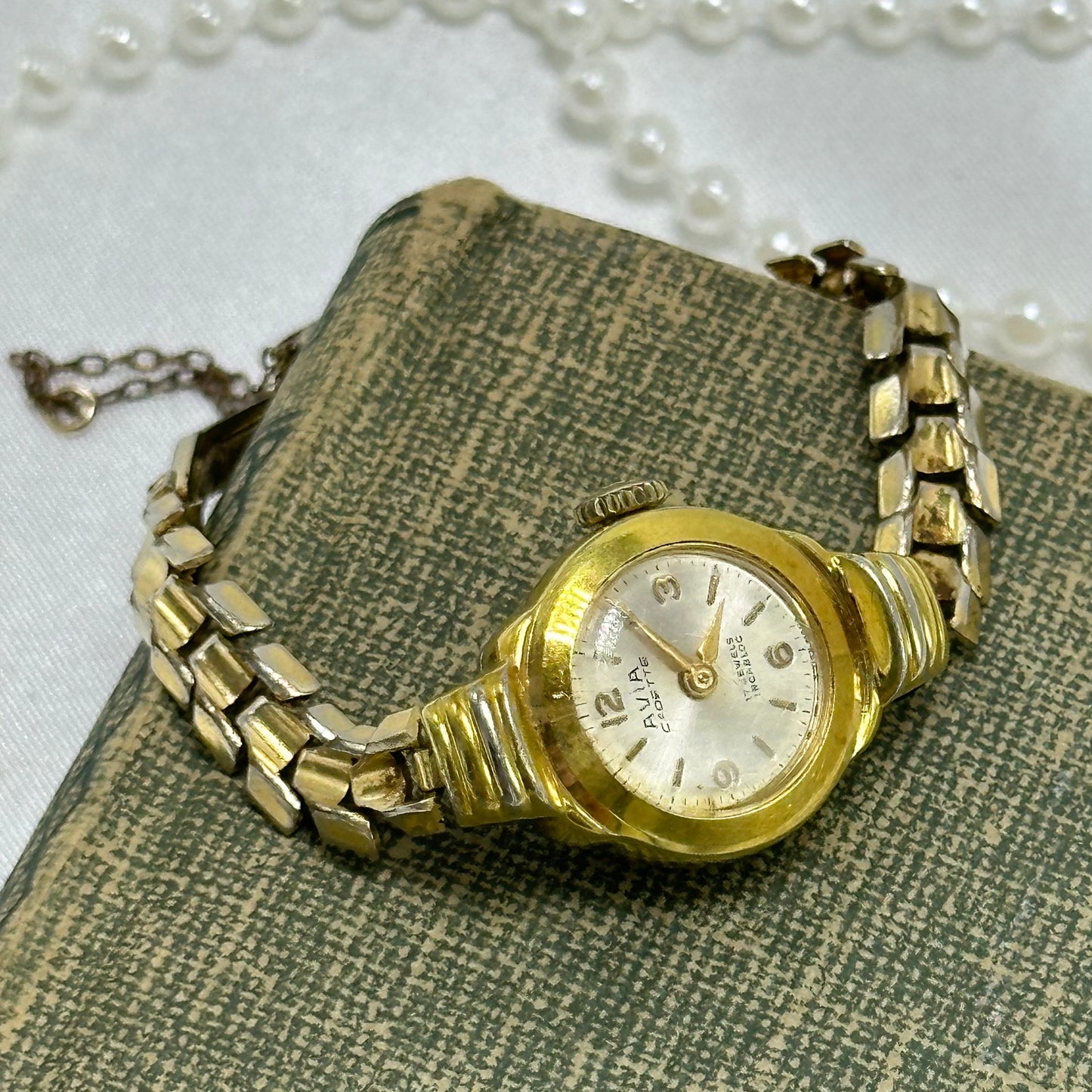 Vintage gold tone AVIA Cadette 17 jewels incabloc manual winding Swiss made watch with dainty round dial and safety chain.
