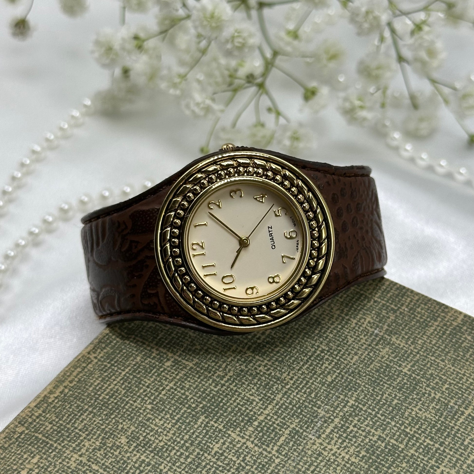 Vintage gold tone Avon cuff watch with brown leather band and quartz movement.