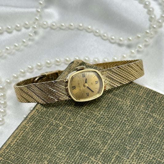 Vintage gold tone Elgin manual winding watch with elegant striped mesh band and Roman Numeral markers.