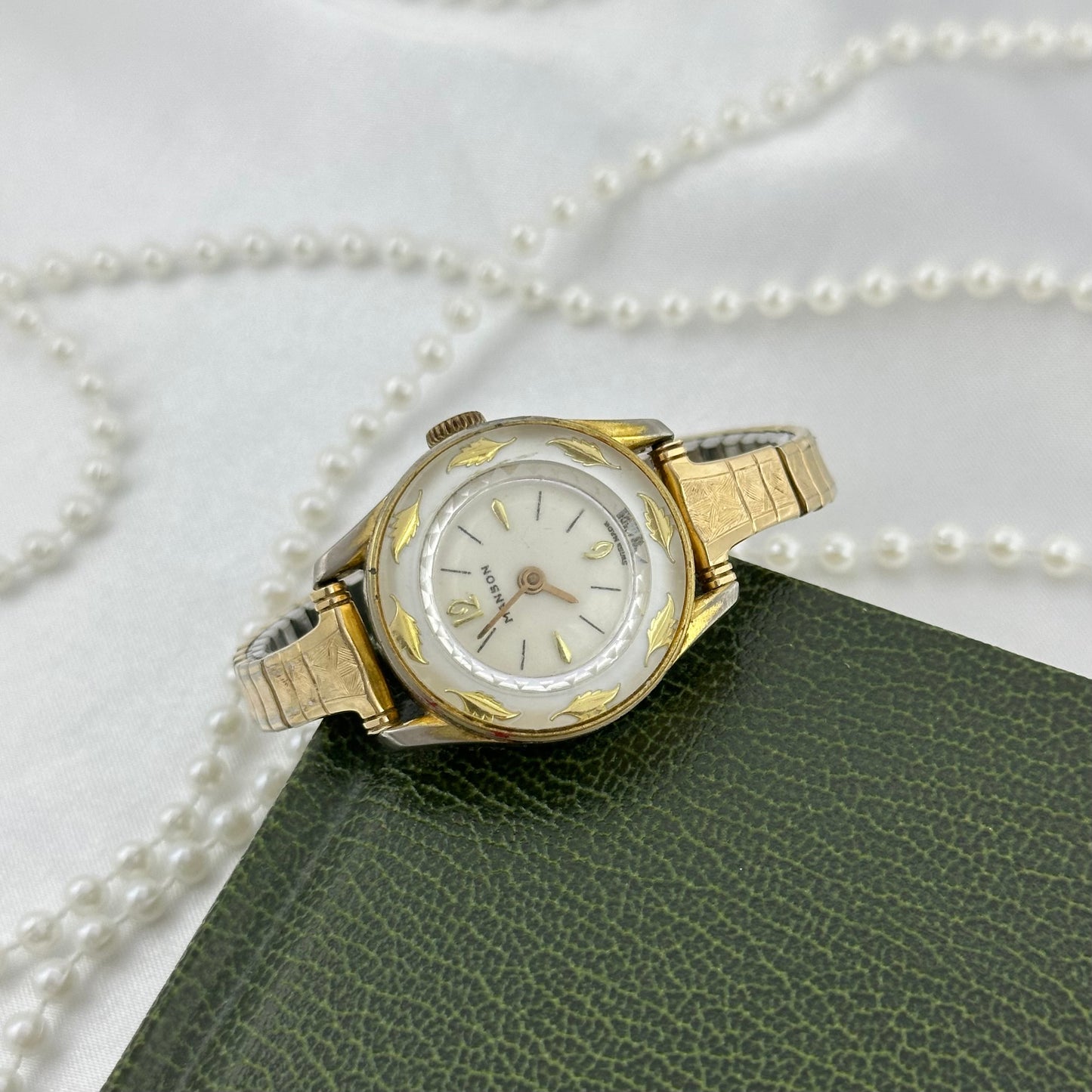 Vintage gold tone Manson manual winding watch with stunning white dial surrounded with golden leaves and stretchable band.