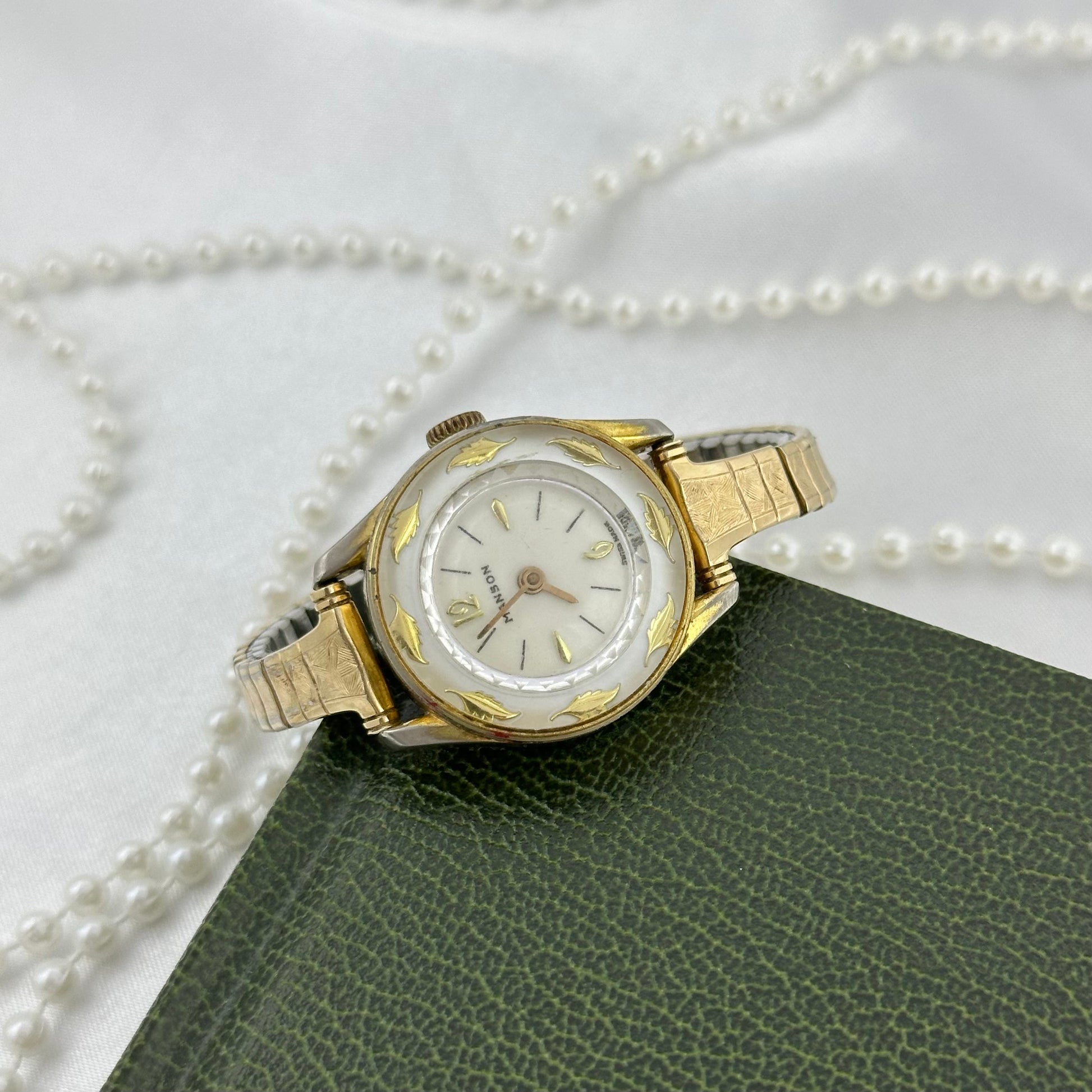 Vintage gold tone Manson manual winding watch with stunning white dial surrounded with golden leaves and stretchable band.