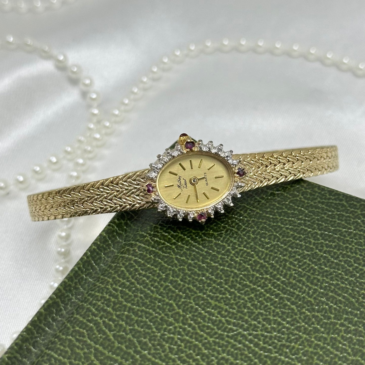 Vintage gold tone Mathey Tissot watch with lab grown diamonds and rubies around a dainty oval dial, slender metal adjustable band, and red jewel crown.