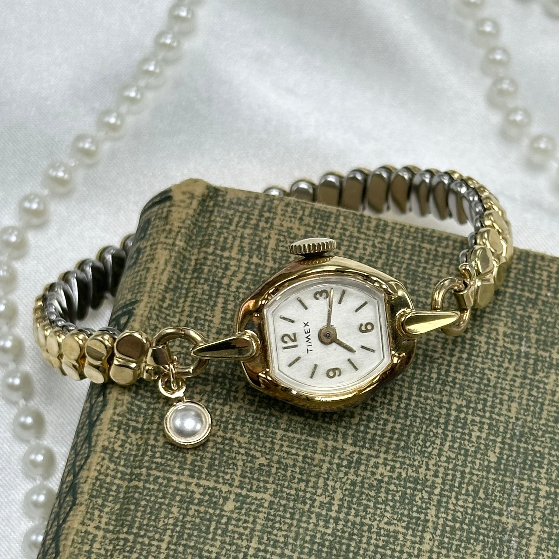 Vintage gold tone Timex manual winding cocktail watch with unique stretchable band and dainty faux pearl charm.