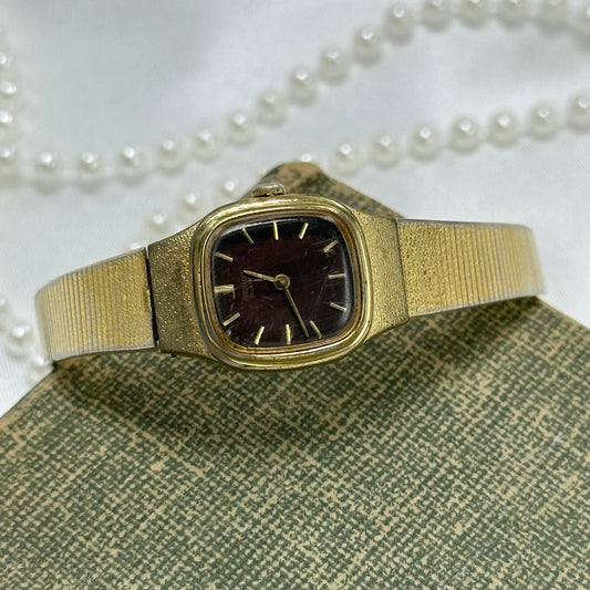 Vintage gold tone dainty Seiko watch with unique brown square dial and clasp band.