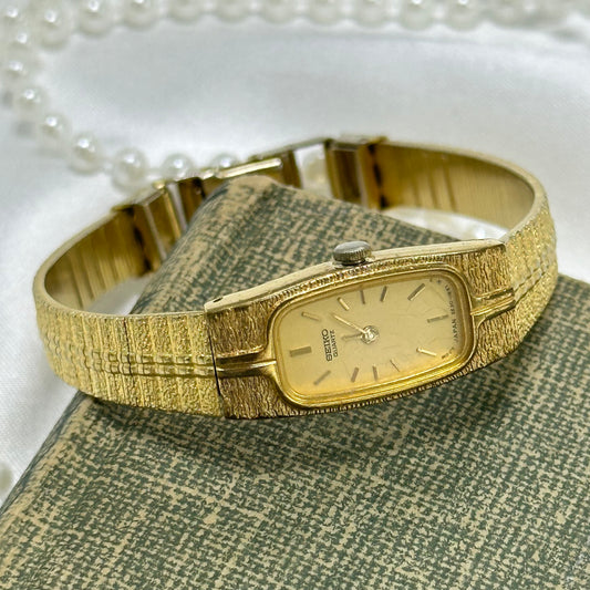 Vintage gold tone dainty Seiko watch with unique textured band and rectangular dial.