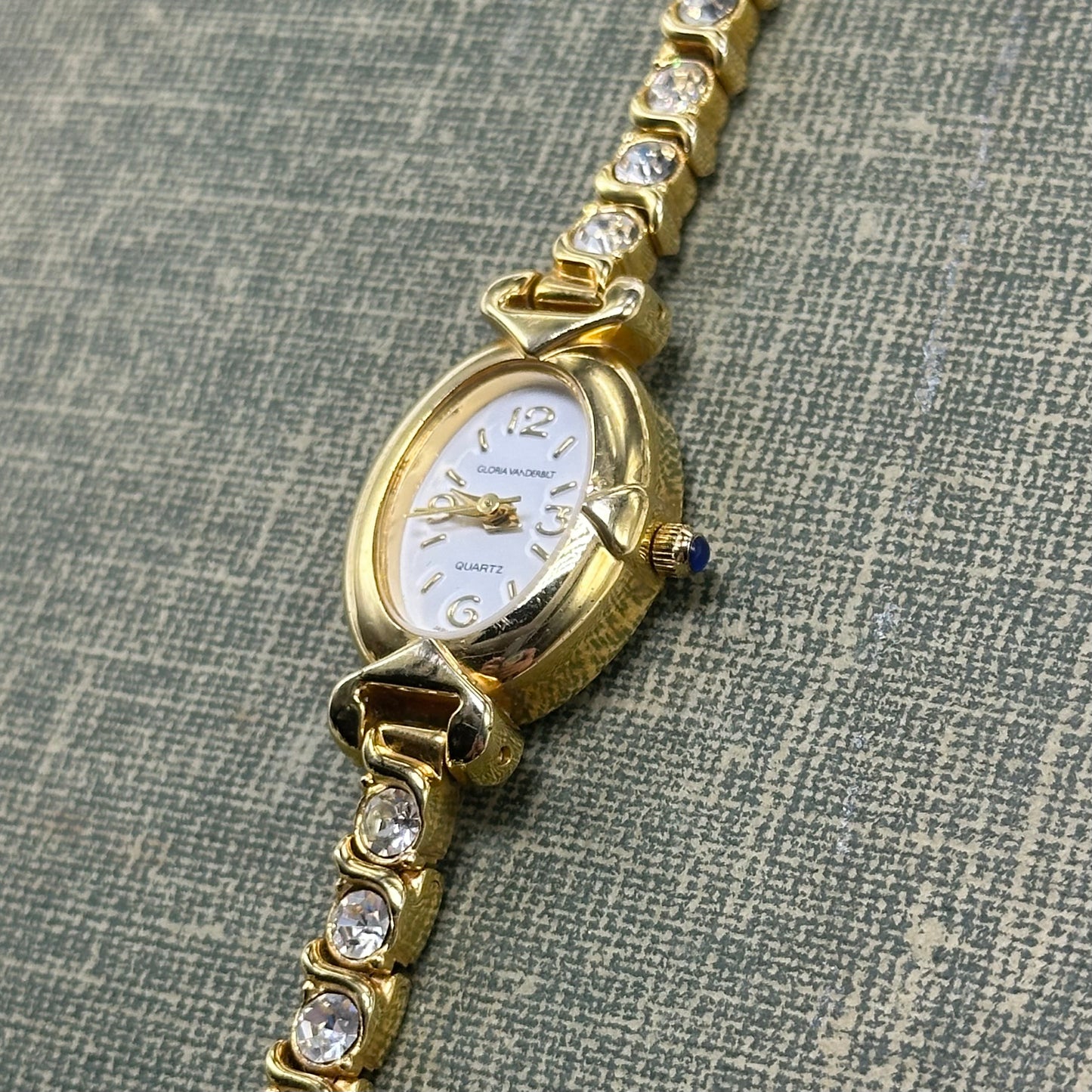 Vintage gold tone diamanté Gloria Vanderbilt watch with clasp band and blue gem crown.