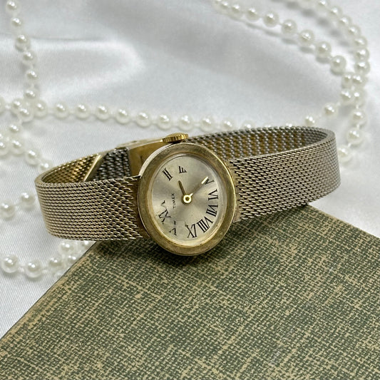 Vintage gold tone mechanical winding Timex watch with mesh band and round dial.
