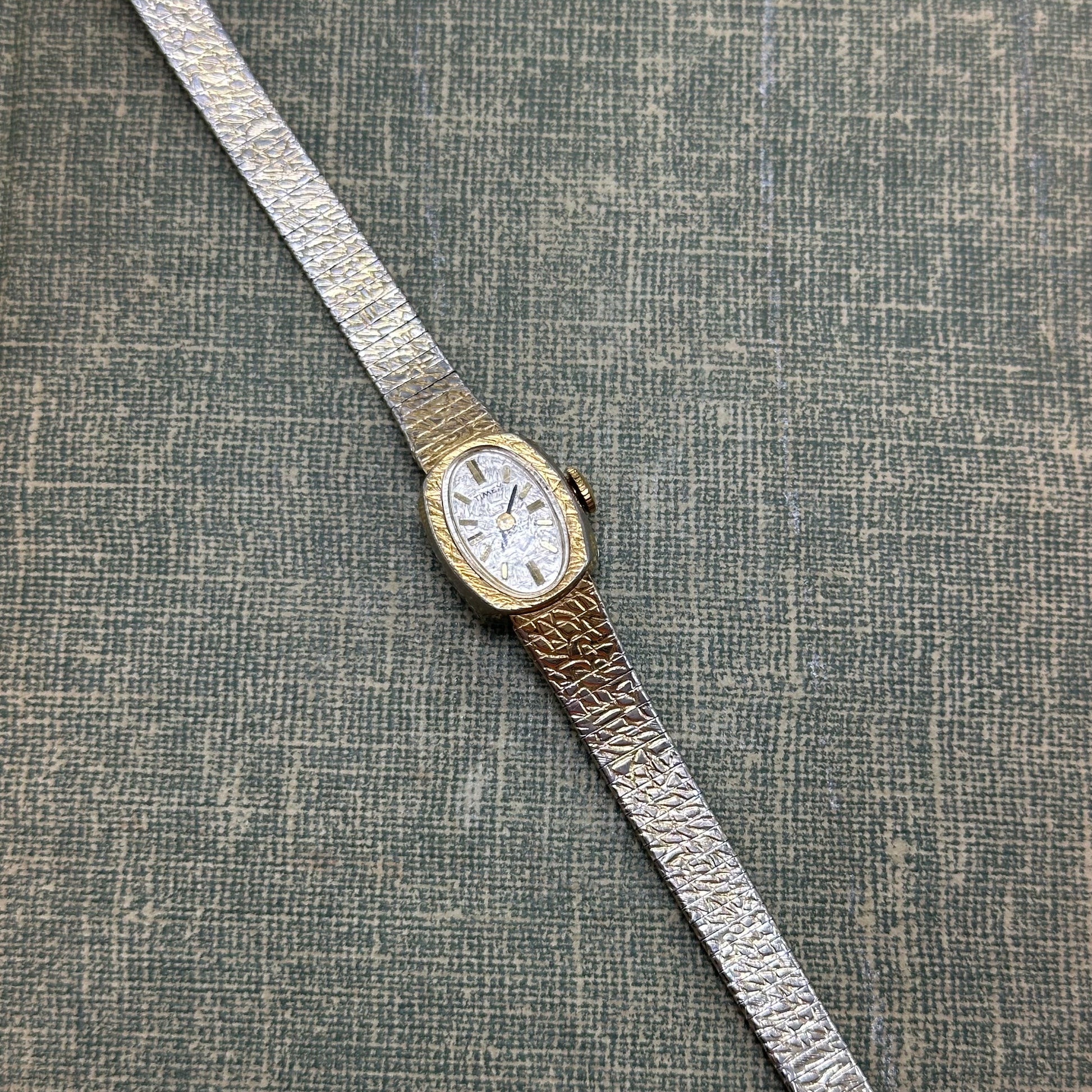 Vintage gold tone mechanical winding Timex watch with oval dial and clasp band.