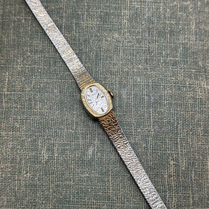 Vintage gold tone mechanical winding Timex watch with oval dial and clasp band.